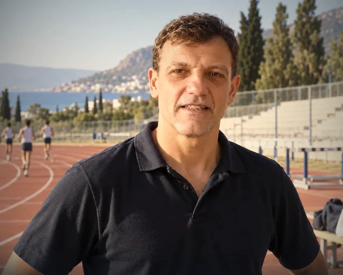 Nikos Moumouris standing beside a running track with hurdles in the background